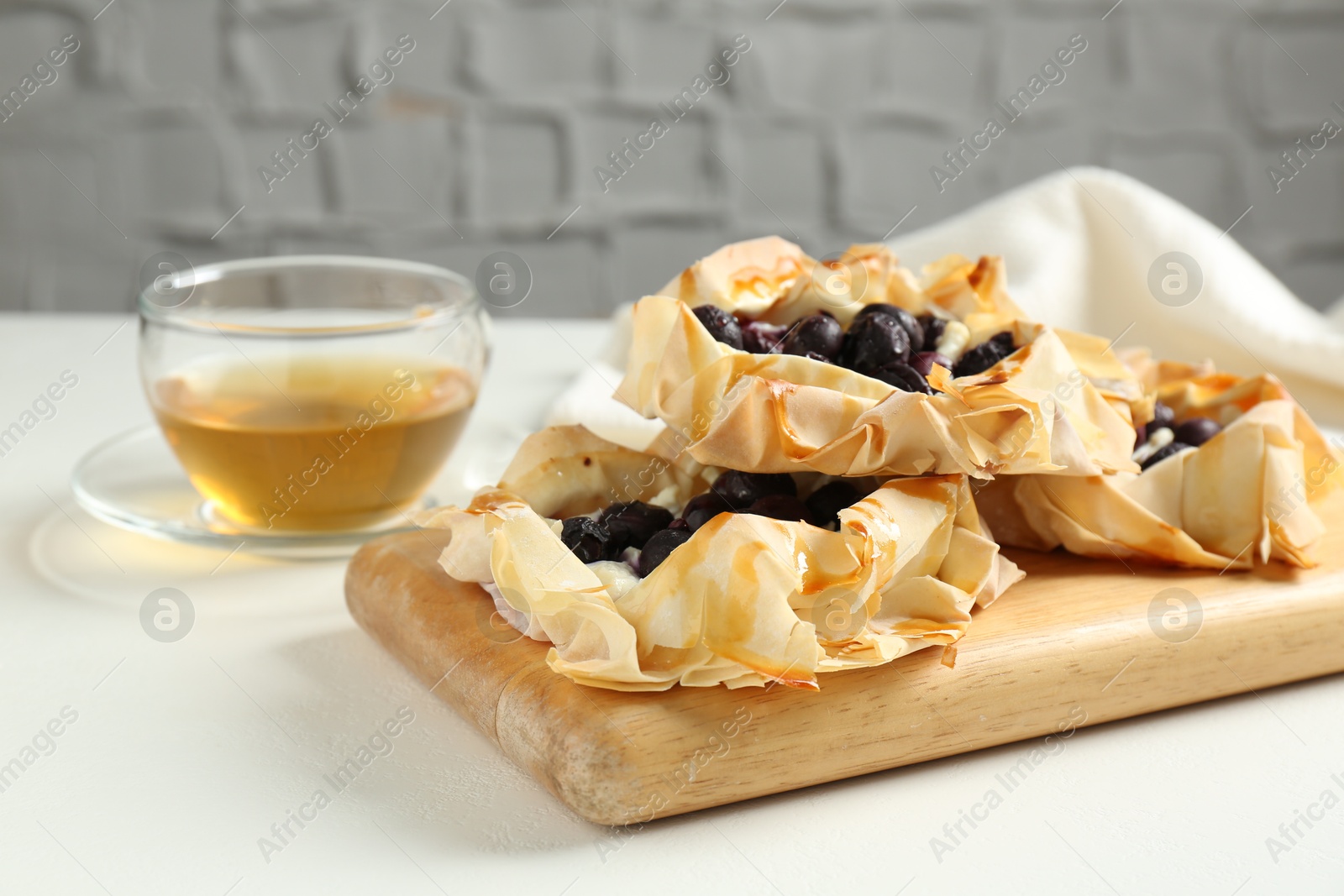 Photo of Delicious puff pastries with blueberries and tea on white table