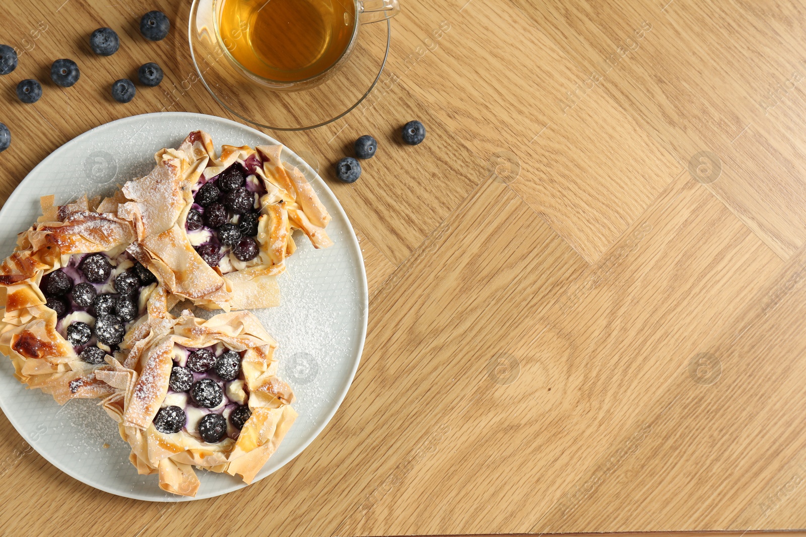 Photo of Delicious puff pastries with blueberries and tea on wooden table, flat lay. Space for text