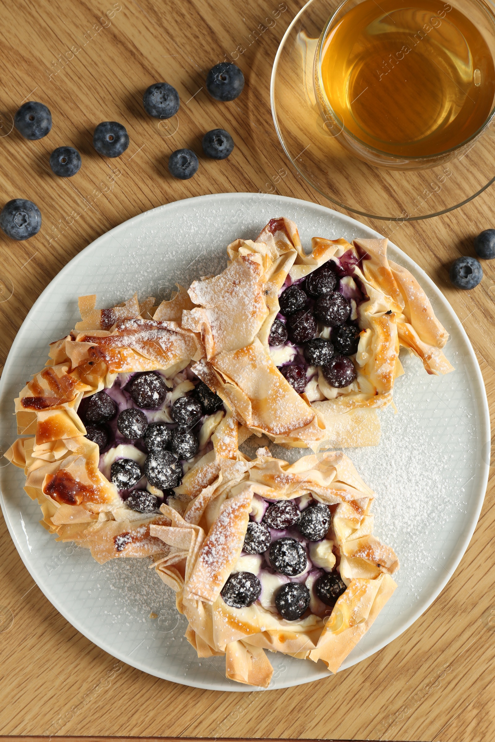 Photo of Delicious puff pastries with blueberries and tea on wooden table, flat lay