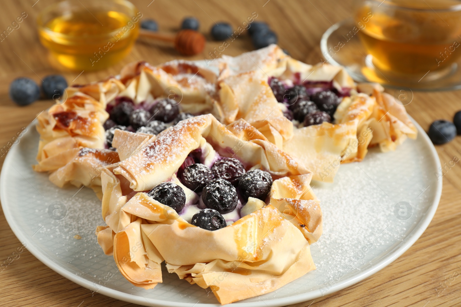 Photo of Delicious puff pastries with blueberries and tea on wooden table, closeup