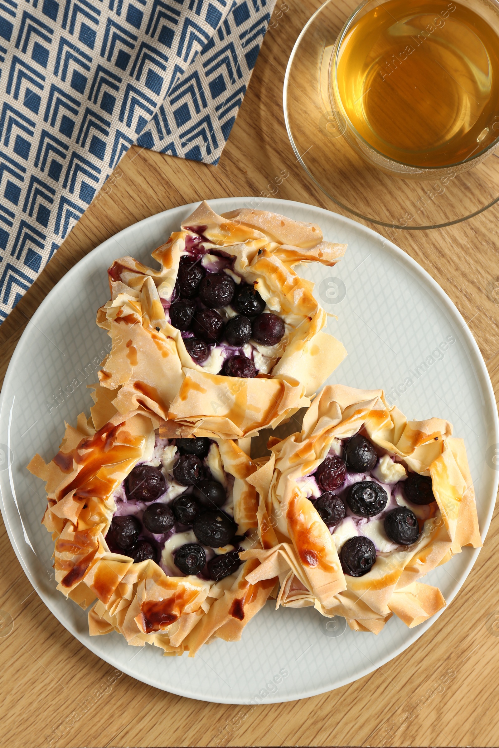 Photo of Delicious puff pastries with blueberries and tea on wooden table, flat lay