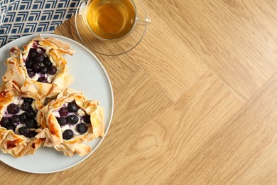 Photo of Delicious puff pastries with blueberries and tea on wooden table, flat lay. Space for text