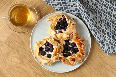 Photo of Delicious puff pastries with blueberries and tea on wooden table, flat lay