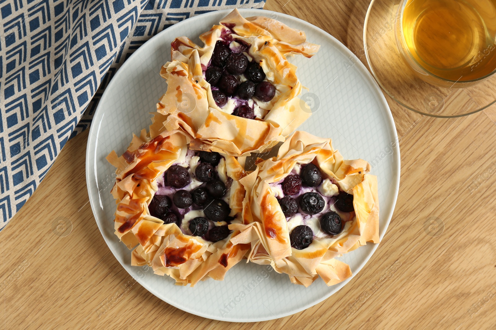 Photo of Delicious puff pastries with blueberries and tea on wooden table, flat lay