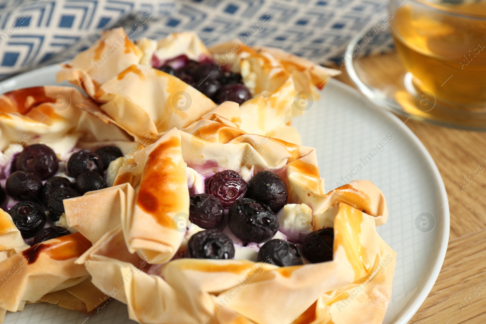 Photo of Delicious puff pastries with blueberries and tea on wooden table, closeup