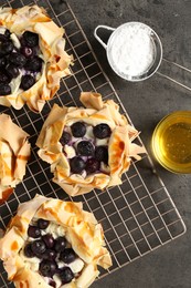 Photo of Delicious puff pastries with blueberries, powdered sugar and honey on gray textured table, flat lay