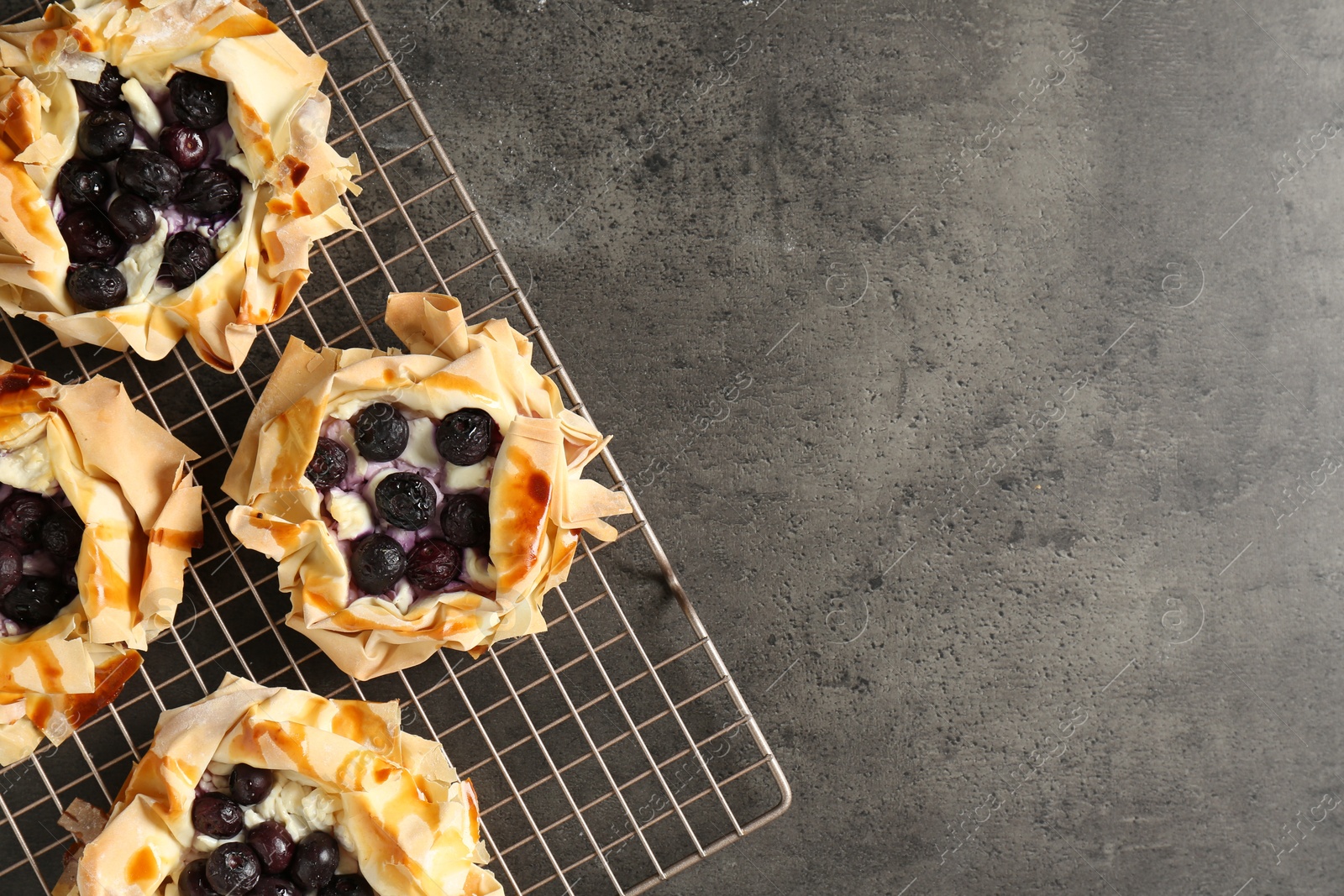 Photo of Delicious puff pastries with blueberries on gray textured table, top view. Space for text