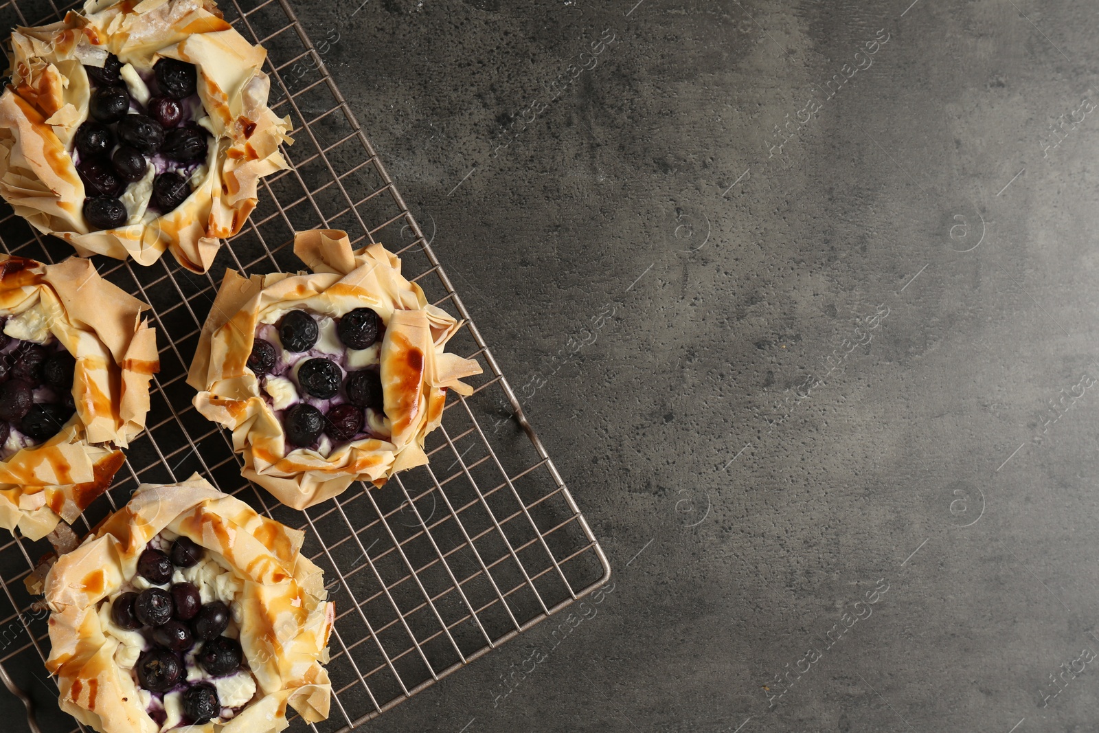 Photo of Delicious puff pastries with blueberries on gray textured table, top view. Space for text