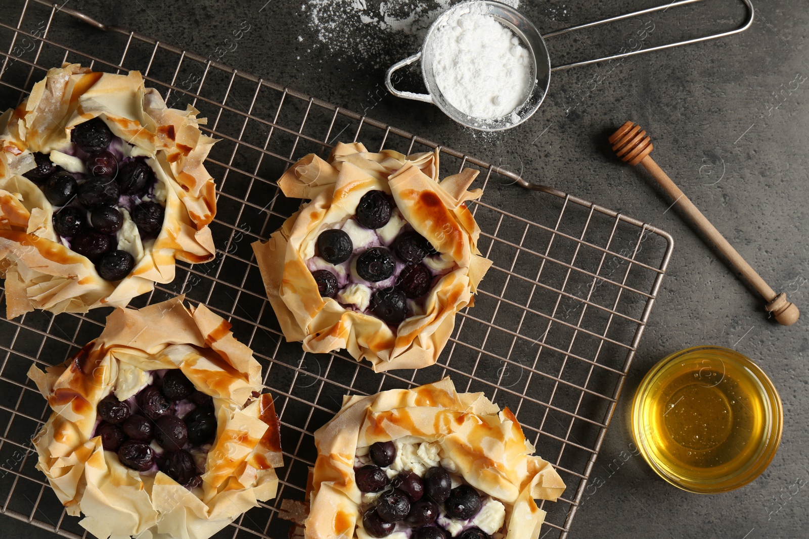 Photo of Delicious puff pastries with blueberries, powdered sugar and honey on gray textured table, flat lay