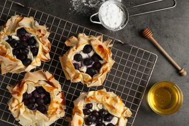 Photo of Delicious puff pastries with blueberries, powdered sugar and honey on gray textured table, flat lay