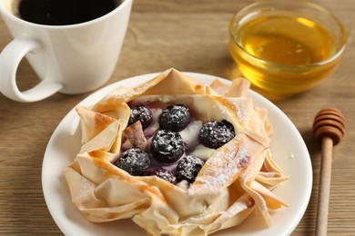 Photo of Tasty puff pastry with blueberries, honey and coffee on wooden table, closeup