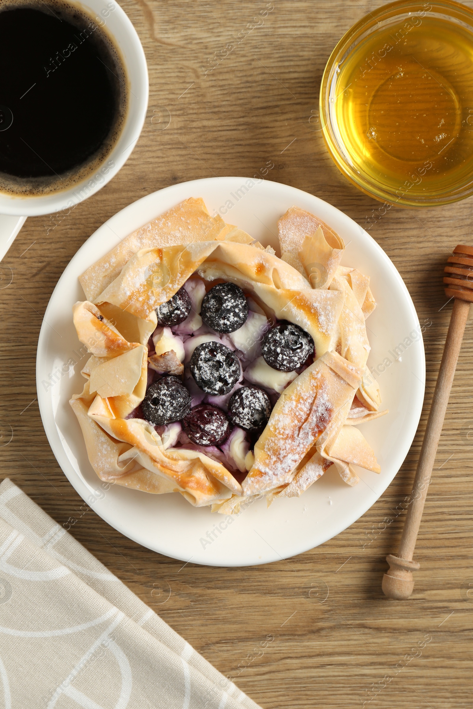 Photo of Tasty puff pastry with blueberries, honey and coffee on wooden table, flat lay