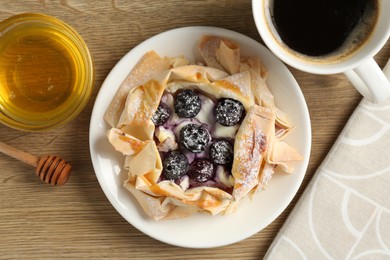 Photo of Tasty puff pastry with blueberries, honey and coffee on wooden table, flat lay