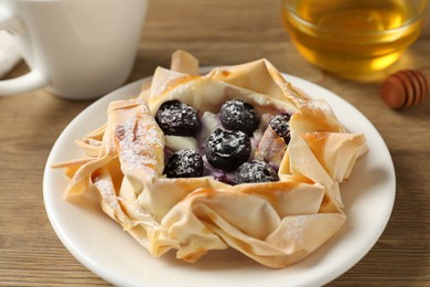 Photo of Tasty puff pastry with blueberries and honey on wooden table, closeup