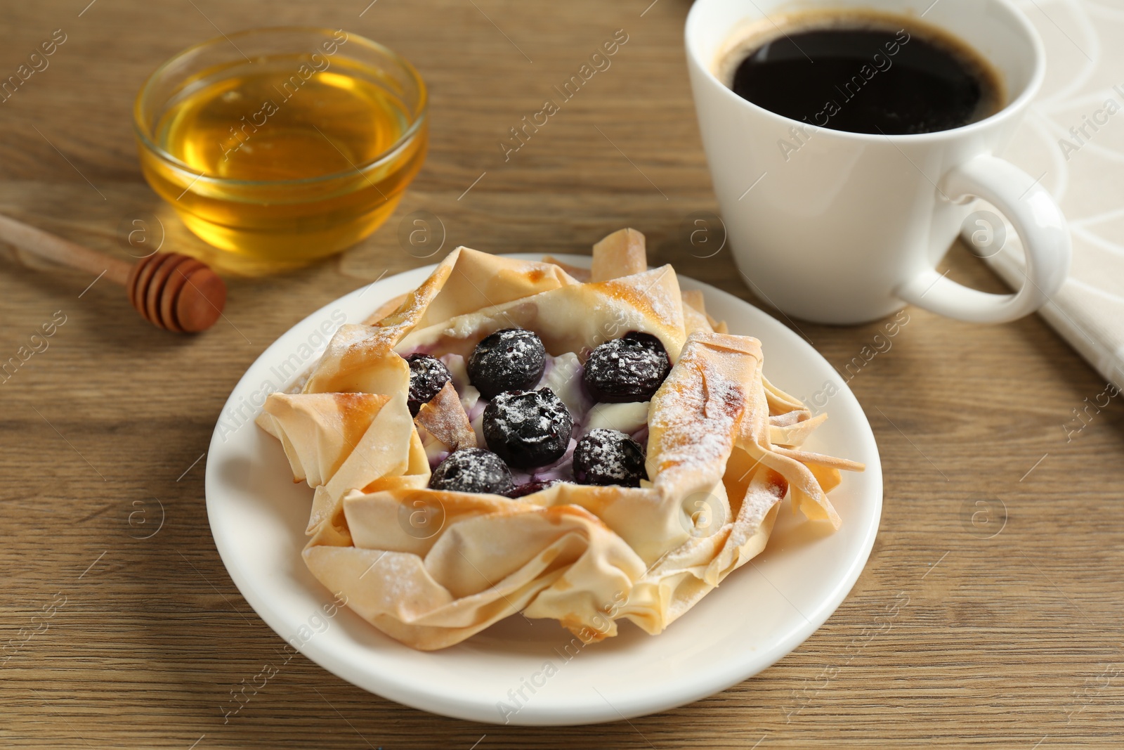 Photo of Tasty puff pastry with blueberries, honey and coffee on wooden table, closeup