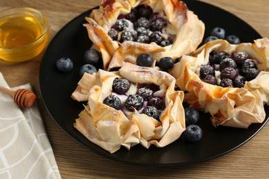 Photo of Tasty puff pastries with blueberries and honey on wooden table, closeup