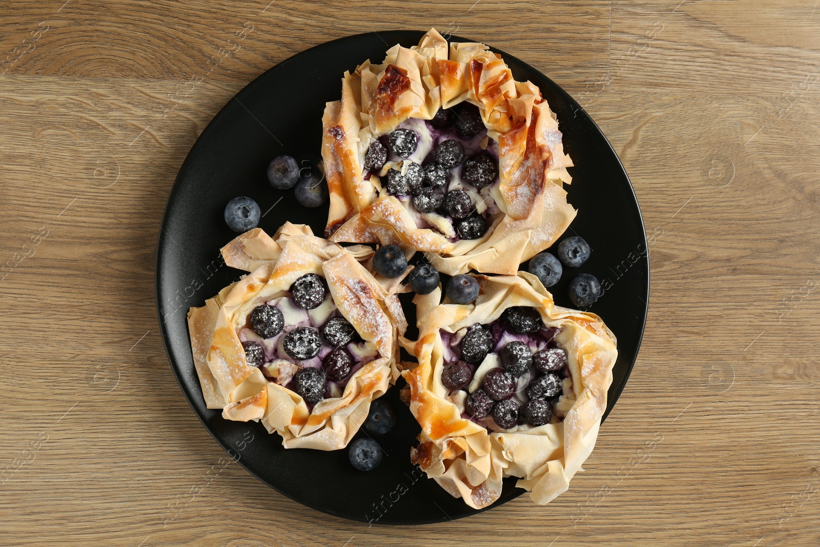 Photo of Tasty puff pastries with blueberries on wooden table, top view