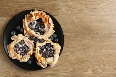 Photo of Tasty puff pastries with blueberries on wooden table, top view. Space for text