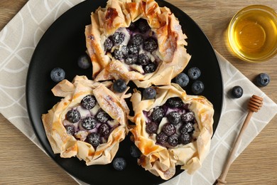 Photo of Tasty puff pastries with blueberries and honey on wooden table, top view