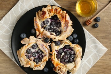 Photo of Tasty puff pastries with blueberries and honey on wooden table, top view