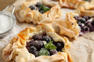 Photo of Tasty puff pastries with blueberries, powdered sugar and mint on table, closeup