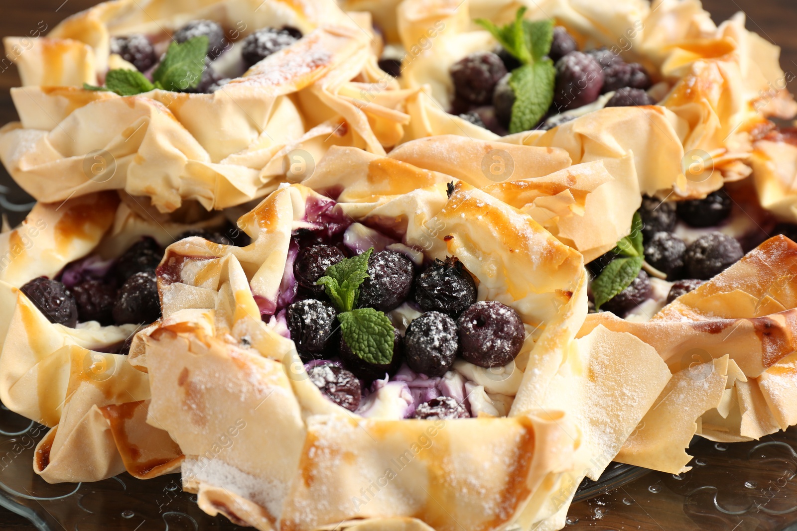 Photo of Tasty puff pastries with blueberries, powdered sugar and mint on plate, closeup