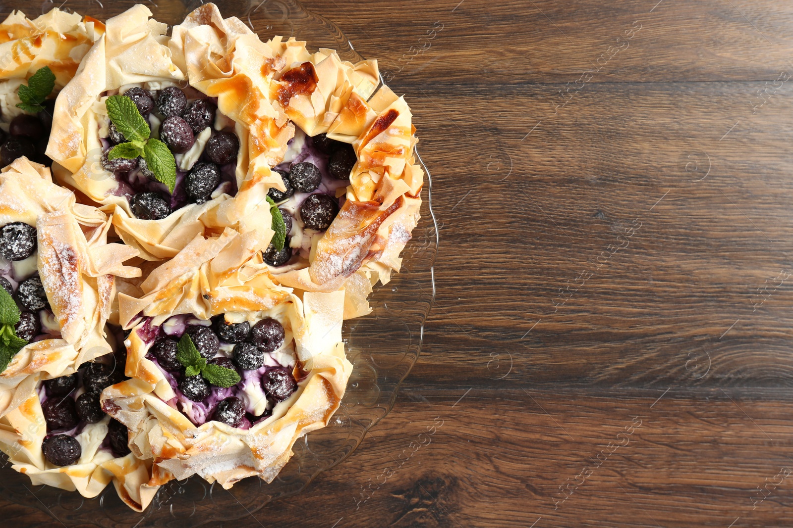 Photo of Tasty puff pastries with blueberries, powdered sugar and mint on wooden table, top view. Space for text