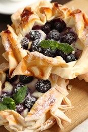 Photo of Tasty puff pastries with blueberries, powdered sugar and mint on table, closeup