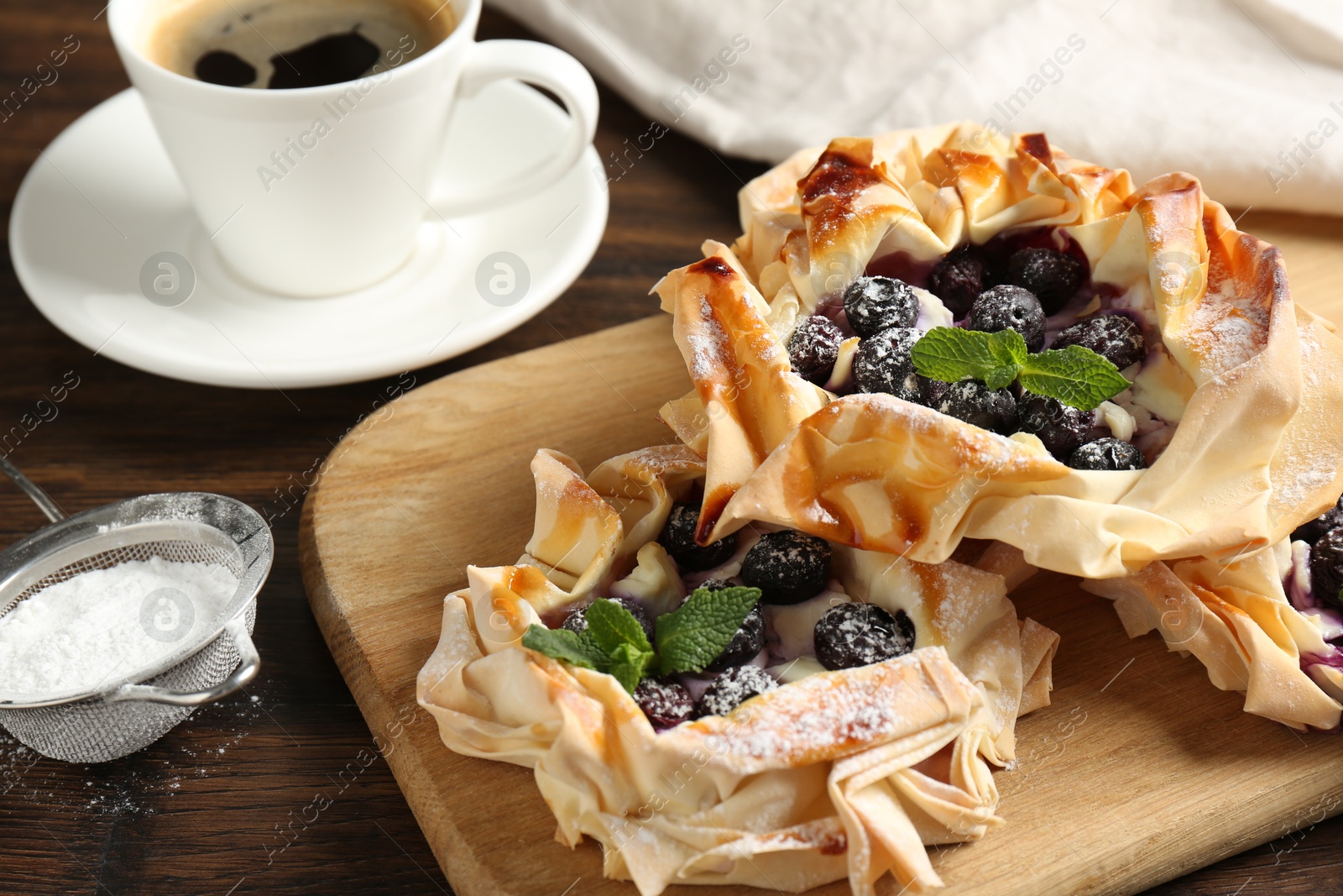 Photo of Tasty puff pastries with blueberries, powdered sugar, mint and coffee on wooden table, closeup