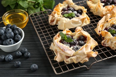 Photo of Tasty puff pastries with blueberries, powdered sugar, mint and honey on dark table, closeup