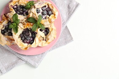 Photo of Tasty puff pastries with blueberries, powdered sugar and mint on white table, top view. Space for text