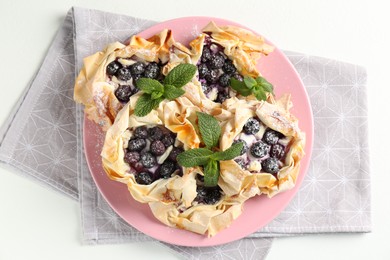 Photo of Tasty puff pastries with blueberries, powdered sugar and mint on white table, top view