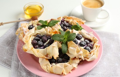 Photo of Tasty puff pastries with blueberries, powdered sugar, mint, honey and coffee on white table, closeup