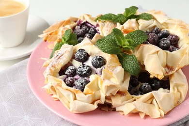 Photo of Tasty puff pastries with blueberries, powdered sugar, mint and coffee on table, closeup