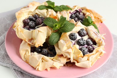 Photo of Tasty puff pastries with blueberries, powdered sugar and mint on table, closeup