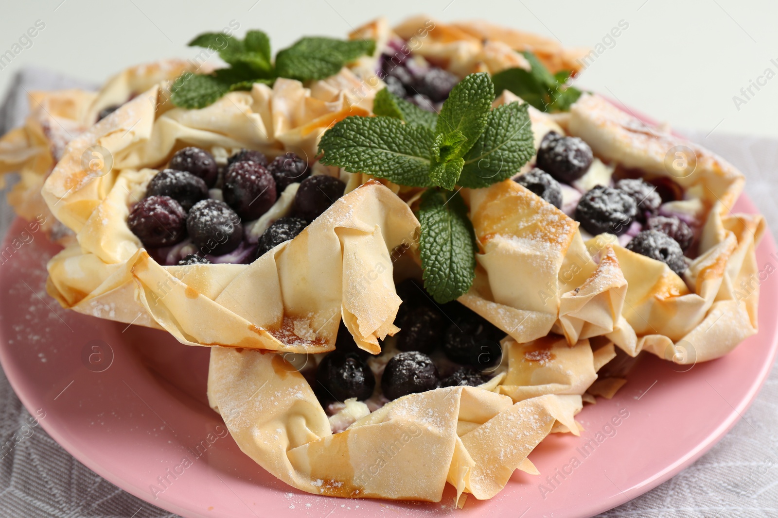 Photo of Tasty puff pastries with blueberries, powdered sugar and mint on table, closeup