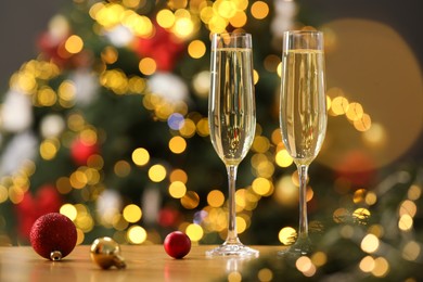 Photo of Champagne in glasses and festive ornaments on wooden table against blurred Christmas lights, space for text. Bokeh effect