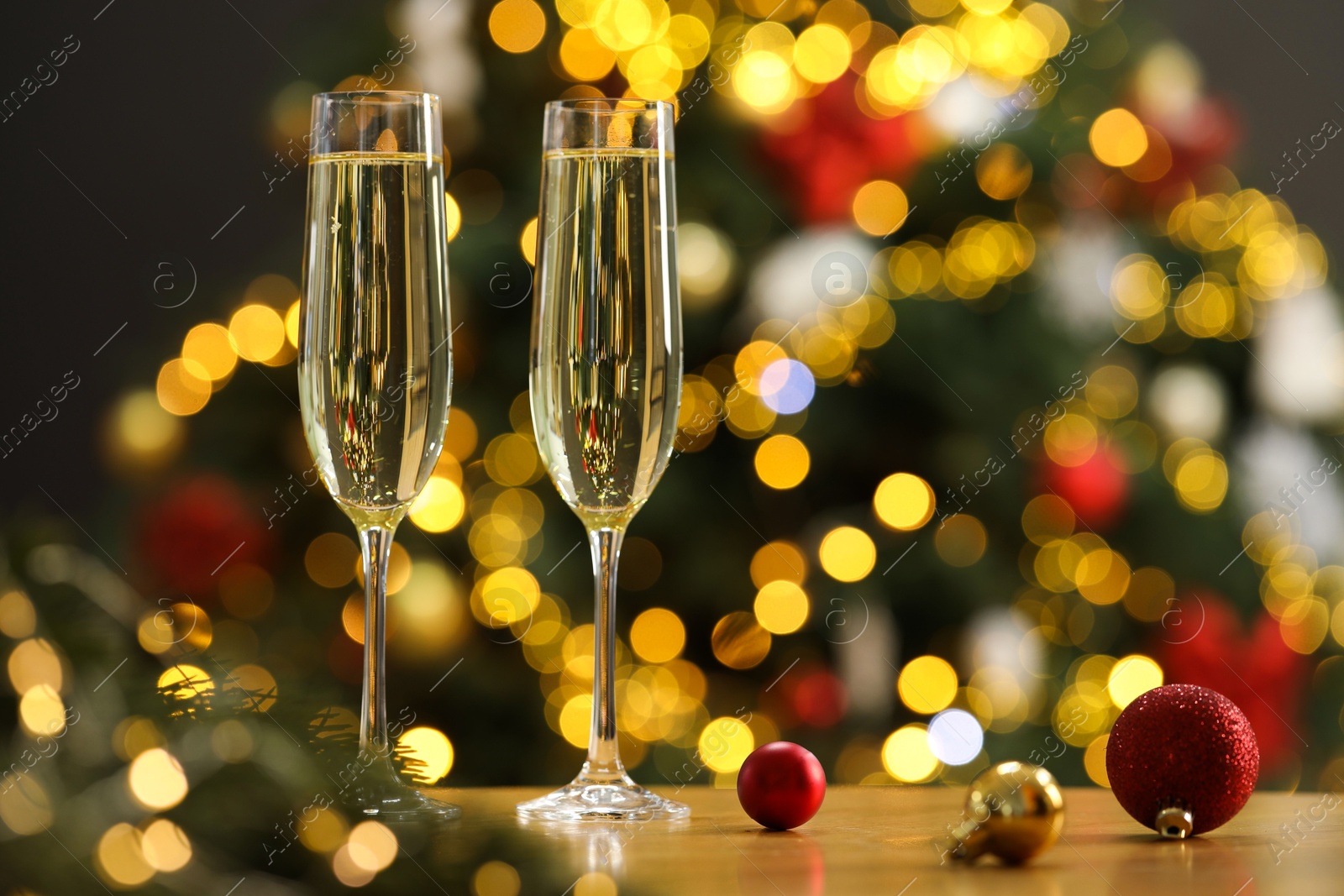 Photo of Champagne in glasses and festive ornaments on wooden table against blurred Christmas lights, space for text. Bokeh effect