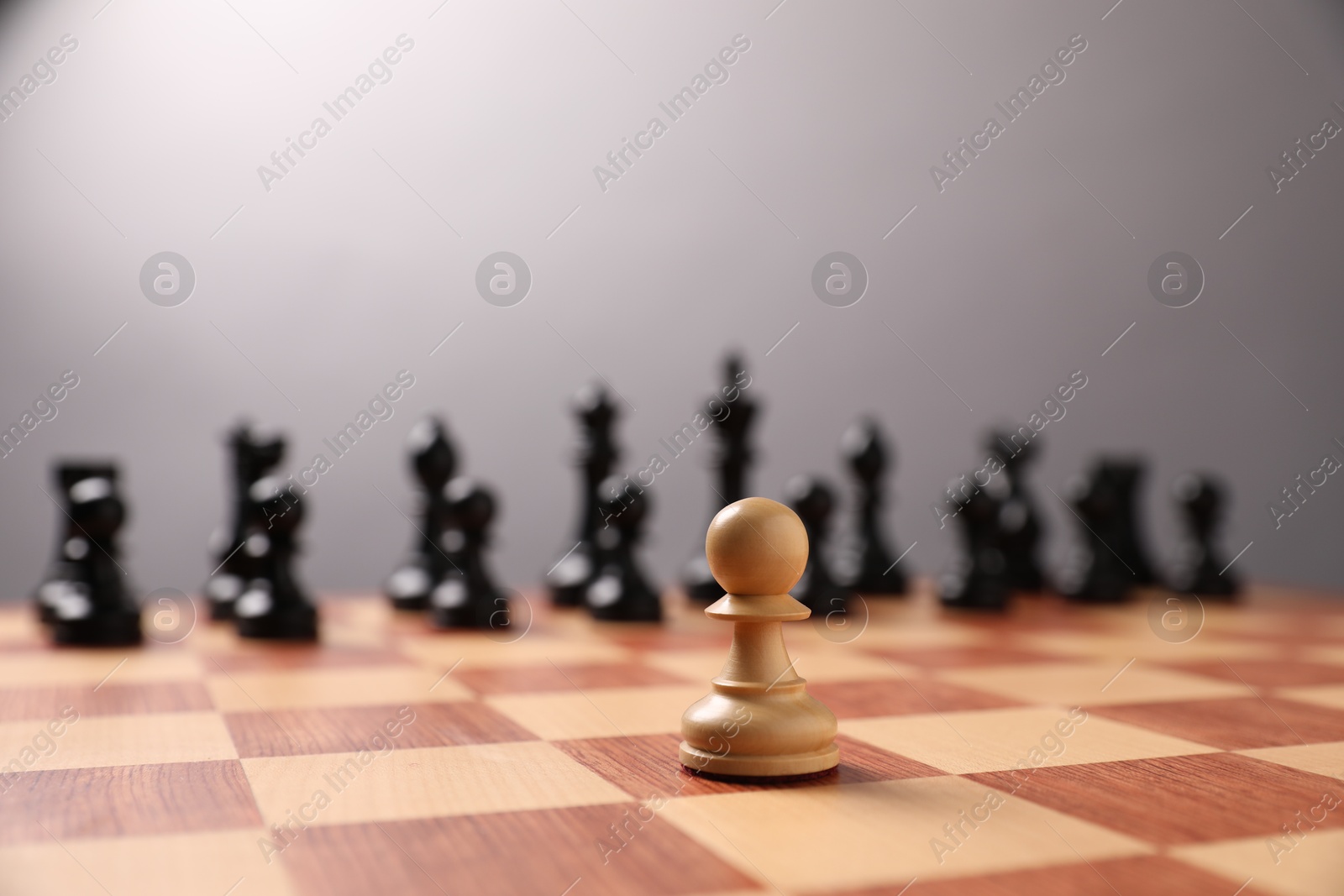 Photo of White pawn in front of other black chess pieces on chessboard, closeup. Competition concept