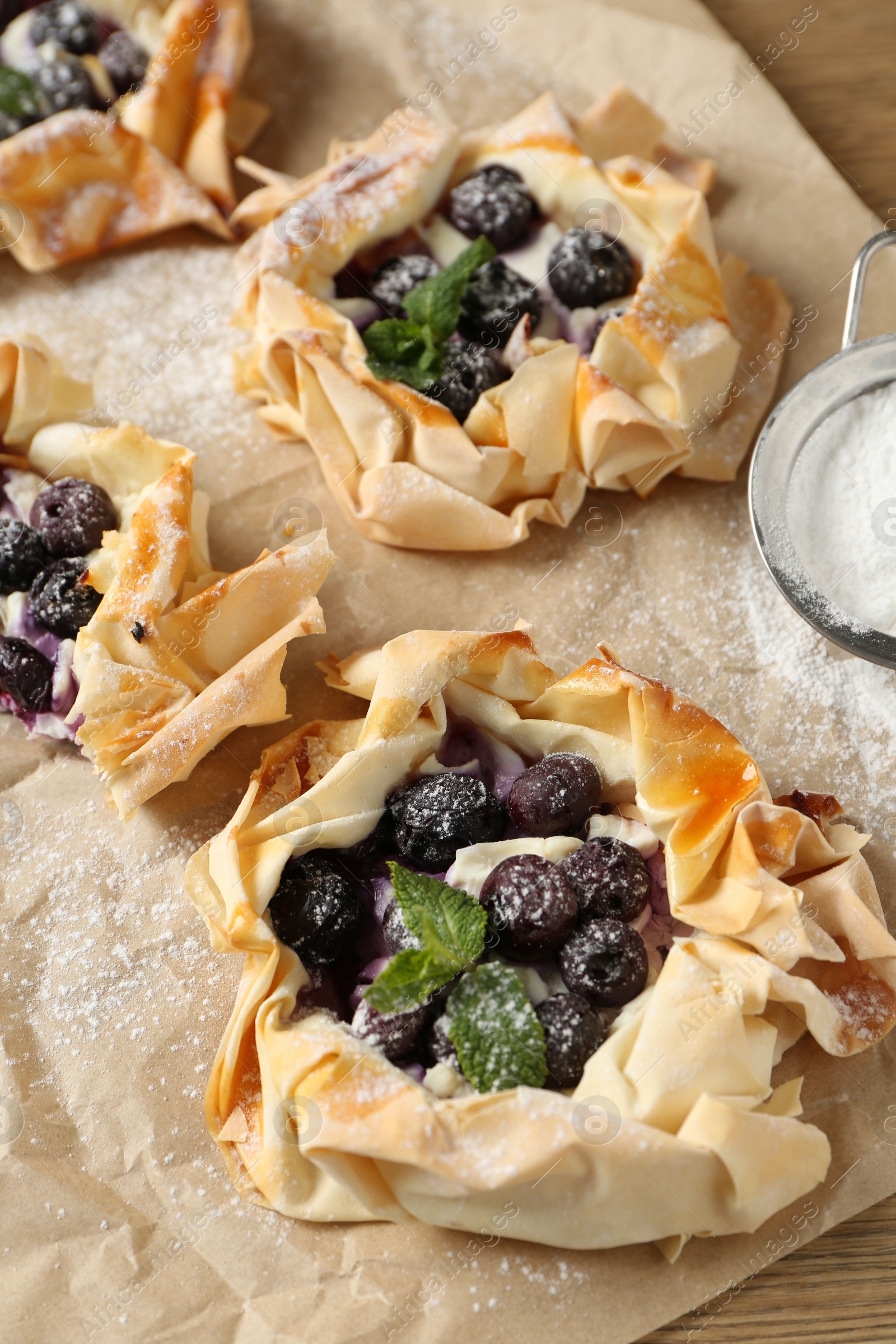 Photo of Tasty puff pastries with blueberries, powdered sugar and mint on table, closeup