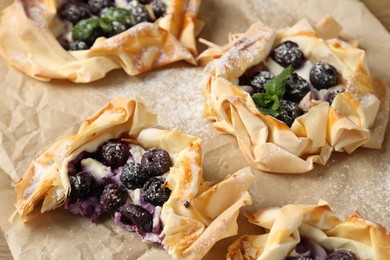 Photo of Tasty puff pastries with blueberries, powdered sugar and mint on table, closeup