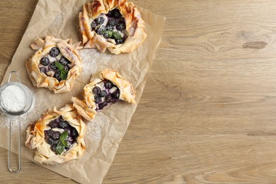 Photo of Tasty puff pastries with blueberries, powdered sugar and mint on wooden table, flat lay. Space for text