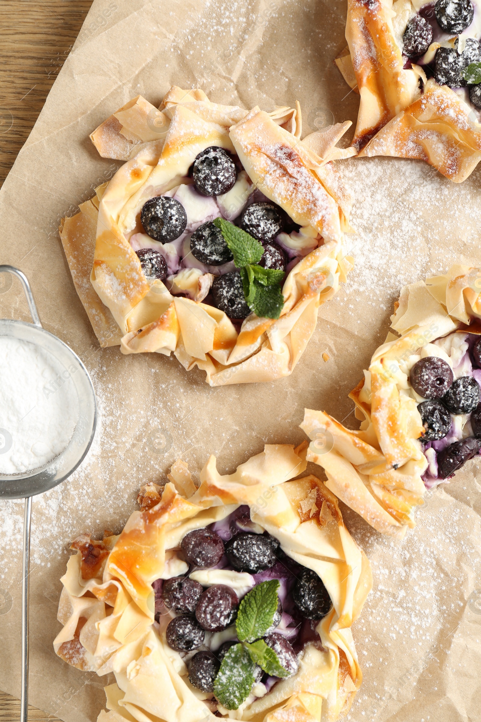 Photo of Tasty puff pastries with blueberries, powdered sugar and mint on table, flat lay