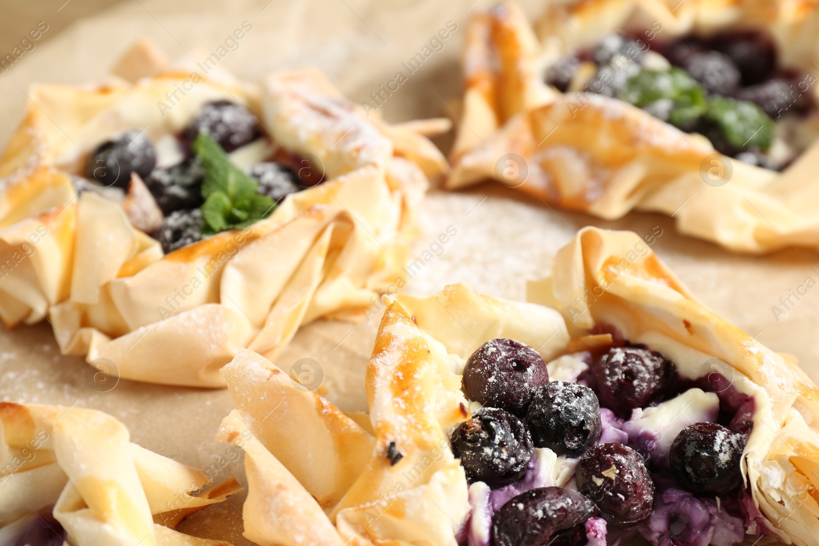 Photo of Tasty puff pastries with blueberries, powdered sugar and mint on table, closeup