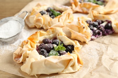 Photo of Tasty puff pastries with blueberries, powdered sugar and mint on table, closeup