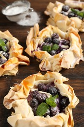 Photo of Tasty puff pastries with blueberries, powdered sugar and mint on wooden table, closeup