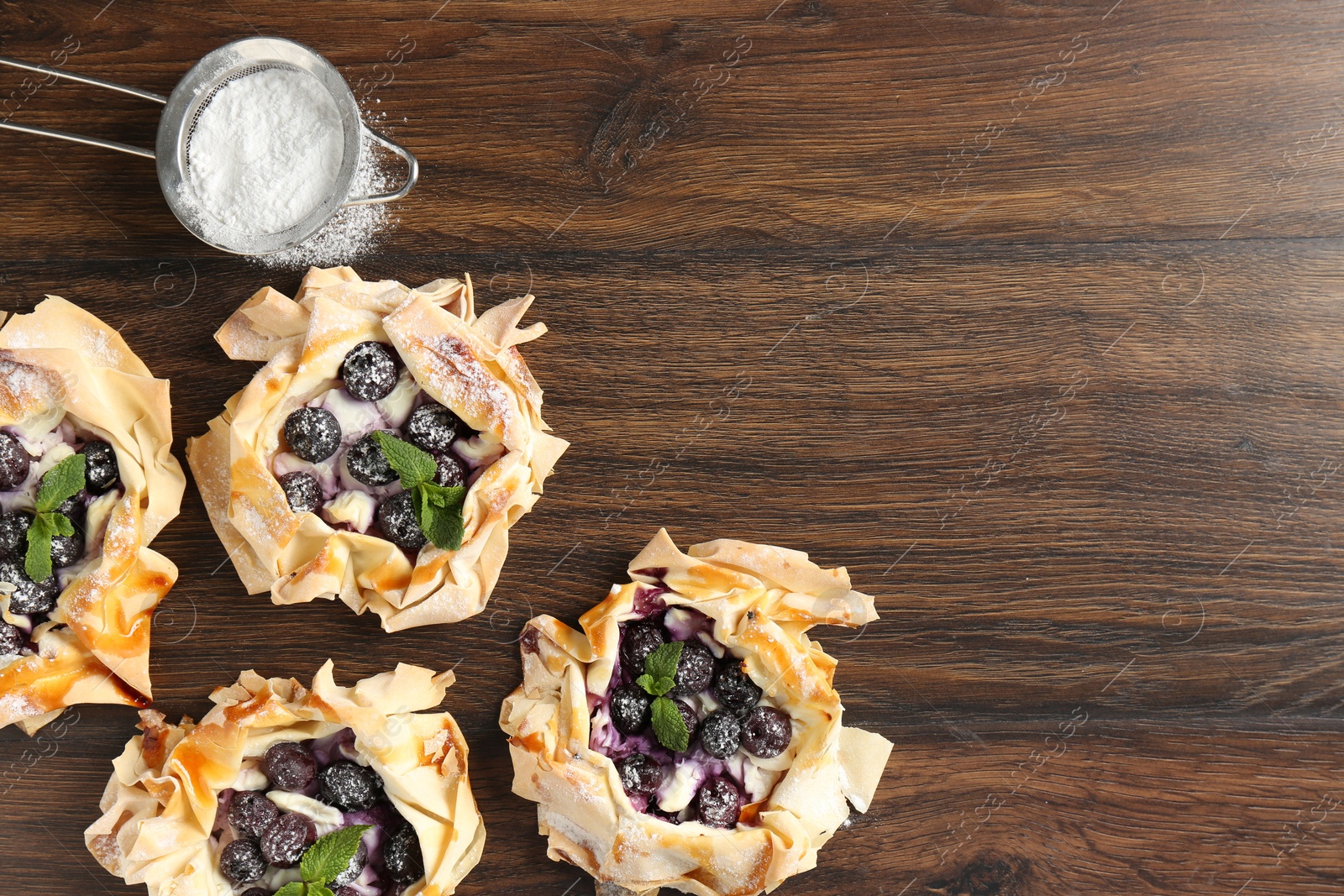 Photo of Tasty puff pastries with blueberries, powdered sugar and mint on wooden table, flat lay. Space for text