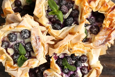 Photo of Tasty puff pastries with blueberries, powdered sugar and mint on plate, top view