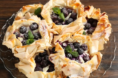 Photo of Tasty puff pastries with blueberries, powdered sugar and mint on wooden table, closeup