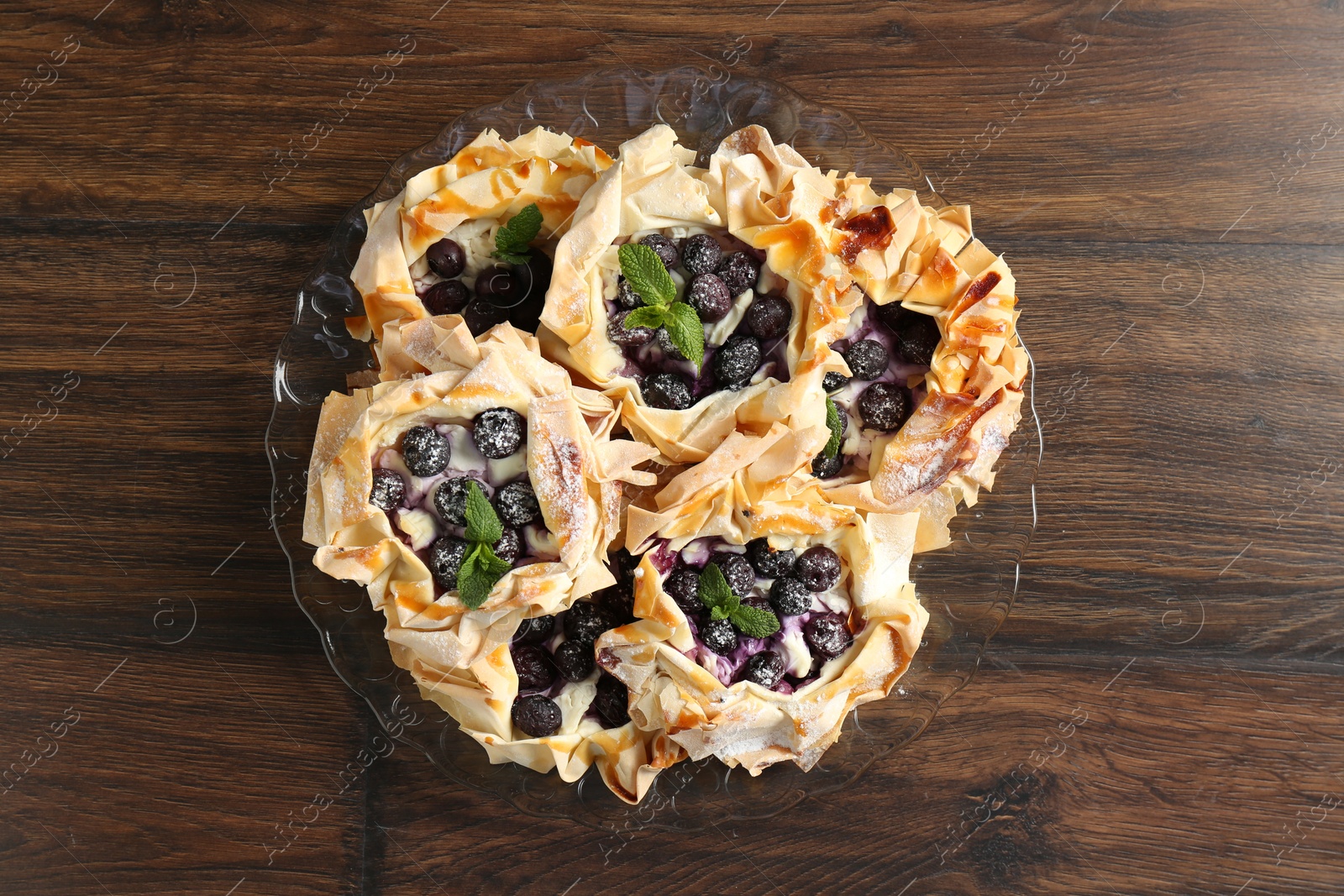 Photo of Tasty puff pastries with blueberries, powdered sugar and mint on wooden table, top view